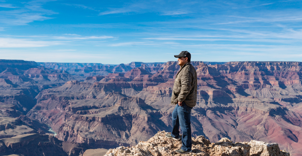 man standing near the edge of the grand canyon with springtime blue skies in the background