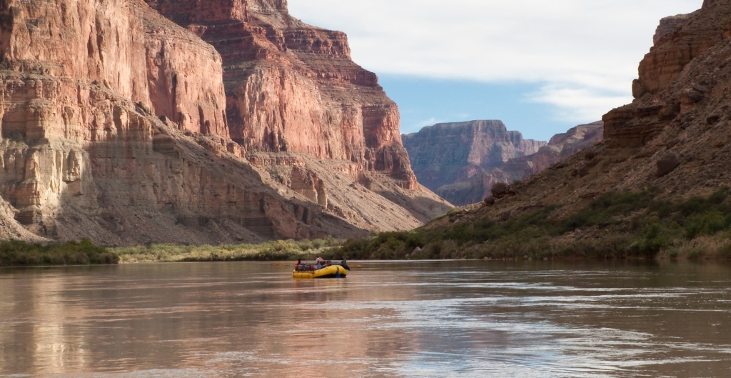 yellow raft floating down the colorado river in the grand canyon